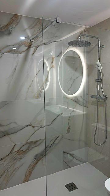 Ducha con revestimiento de mármol veteado y espejo LED ovalado retroiluminado